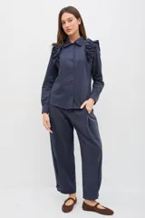 Camisa de gabardina de tencel color negro, con cuello clásico, cierre frontal de botones y volados fruncidos en los hombros.