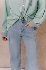Pantalón de jean color arena con silueta wide leg, tiro medio-alto y costuras verticales delanteras que estilizan la figura. Cuenta con bolsillos funcionales y cierre frontal con doble botón.