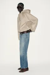 Chaqueta bomber de efecto ante en color marrón, con capucha ajustable mediante cordones, cierre frontal con cremallera, bolsillos laterales y bajo con elástico interior.