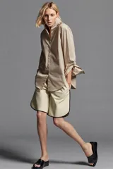 Camisa oversize color beige con mezcla de algodón, cuello smoking, manga larga con puños anchos y cierre frontal con botones ocultos por solapa.