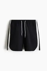Short deportivo negro con bandas laterales blancas, cintura elástica con cordón ajustable blanco y bolsillos laterales.