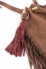 Charm para bolso compuesto por flecos de cuero sintético color marrón, decorados con pequeñas tachas metálicas doradas. Incluye un aro y un cierre de mosquetón metálico en tono dorado.