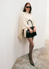 Poncho de tejido de punto color marfil, con cuello alto vuelto y diseño amplio con aberturas para los brazos.