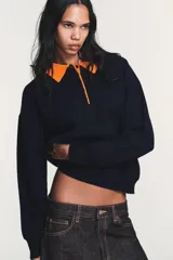 Jersey de punto de manga larga con cuello tipo polo en color naranja a contraste. Presenta cierre frontal con botones y diseño de corte holgado.