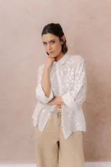 Camisa blanca de calce relajado con tejido semitransparente y bordados florales en relieve. Cuenta con cuello camisero, abotonadura frontal y mangas amplias.