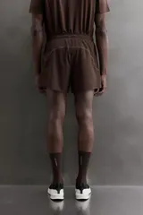 Short de running color marrón, confeccionado en tejido técnico elástico con forro interior. Cuenta con cintura elástica ajustable, bolsillos laterales con cierre de cremallera oculto y aberturas en las perneras.