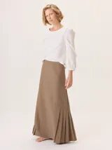 Falda larga color marrón, con diseño de corte asimétrico y tablas en el ruedo que aportan movimiento. Confeccionada en una mezcla de algodón y tencel.