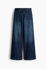 Jean wide leg de tiro alto en denim de algodón azul, con costuras frontales verticales y bolsillos simulados con solapa y botones en la parte delantera.