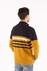 Buzo tejido de punto con medio cierre frontal, diseño de bloques de color en azul marino, blanco y mostaza. Presenta cuello alto, mangas largas con puños acanalados y logo bordado en el pecho.