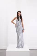 Vestido largo de fiesta color plateado con acabado metalizado, escote halter con detalle de nudo y espalda descubierta.