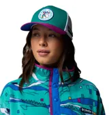 Gorra Columbia x Disney tipo trucker, con panel frontal de color verde, visera fucsia, paneles traseros de malla blanca y parche redondo con gráfico de Mickey Mouse practicando esquí. Incluye etiqueta lateral con el logo de Columbia y Disney.