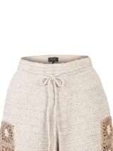 Short tejido a crochet de color beige con detalles geométricos en tono marrón en el borde inferior y lateral. Cuenta con cintura elástica y cordón ajustable con borlas.