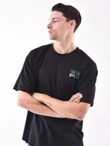 Remera negra de corte oversize con cuello redondo y manga corta. Presenta un pequeño estampado en el pecho con texto en color verde azulado.