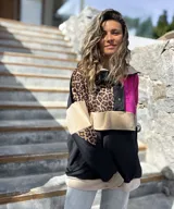 Buzo de estilo canguro con diseño color block que combina paneles en negro, fucsia, beige y un estampado de leopardo. Presenta cuello con cierre de botones a presión y un bolsillo frontal tipo canguro.