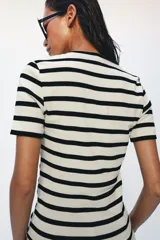 Camiseta de manga corta confeccionada en tejido de algodón con textura rib. Presenta un diseño a rayas horizontales en color blanco y negro, con un escote redondo pronunciado y bajo recto.