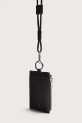 Tarjetero de piel marrón con diseño colgante para el cuello. Cuenta con ranuras para tarjetas, un bolsillo lateral con cierre de cremallera, anilla metálica y cordón largo ajustable.