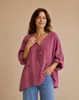 Blusa magenta de lino, con cuello en V, bolsillos frontales aplicados con bordes deshilachados, mangas largas con trabilla para sujetar arremangadas y detalles de botones decorativos con tiritas en el escote.