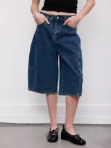 Bermuda de jean de tiro alto, color celeste claro, con diseño amplio y largo por debajo de las rodillas. Cuenta con bolsillos clásicos y costuras pespunteadas en contraste.