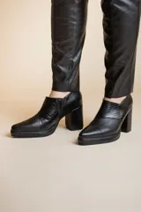Botinetas negras de cuero con puntera fina, detalle de textura en el empeine, cierre lateral con cremallera y tacón cuadrado.