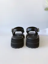 Sandalias negras de cuero con tiras cruzadas, plataforma track y hebilla lateral.