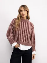Sweater de punto con diseño de trenzas verticales, cuello alto y corte holgado. Presenta mangas largas con puños acanalados y un largo a la cadera.