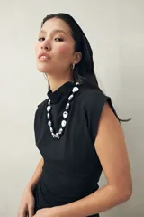 Vestido corto de punto color negro, sin mangas, con cuello cerrado y hombros levemente estructurados. Presenta frunce lateral que realza la figura.