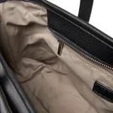 Cartera de mano y hombro color negro, con textura de cuero granulado. Presenta dos asas superiores y una correa larga regulable y desmontable. El frente lleva un aplique rectangular con el logo XL.