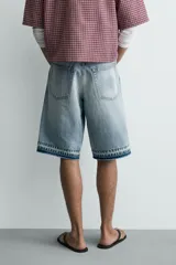 Bermuda de denim de algodón con efecto lavado desgastado en tonos marrones y azules. Tiene tiro medio, diseño de cinco bolsillos, pierna recta de corte holgado y bajo con acabado irregular. Cuenta con cierre frontal de cremallera y botón metálico.