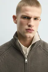 Chaqueta relaxed fit de punto tejido en hilatura con mezcla de algodón, color beige, con cuello subido y manga larga. Cuenta con acabados en rib, efecto lavado y cierre frontal con cremallera.