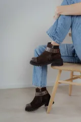 Bota corta de gamuza marrón con puntera de cuero liso, suela track negra y correa desmontable con tachas metálicas.