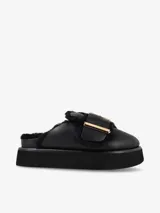 Zueco negro de cuero con plataforma y plantilla recubierta de piel de oveja. Presenta una hebilla dorada de gran tamaño en la capellada.