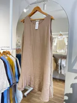 Vestido corto sin mangas, color gris topo, con escote redondo y detalle de volado en el ruedo. El tejido presenta una textura arrugada característica del lino.