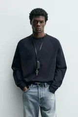 Camiseta de manga larga con cuello redondo, confeccionada en algodón compacto y pesado, con diseño de corte relajado y costuras decorativas en el cuello.