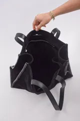 Bolso tipo shopper de gran tamaño, confeccionado en cuero gamuzado color marrón. Presenta estructura rectangular con bordes reforzados en cuero liso oscuro, doble asa de hombro y cierre mediante botón magnético.