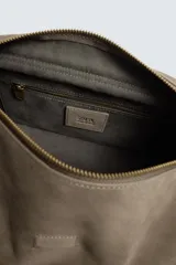 Bandolera de piel con acabado en serraje, diseño rectangular con solapa frontal y cierre magnético. Cuenta con un asa larga ajustable y compartimento interior con cierre de cremallera.