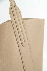 Bolso tipo tote de diseño minimalista, confeccionado en material texturizado color beige, con doble asa larga para llevar al hombro y costuras reforzadas en los laterales.