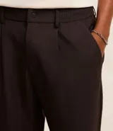 Pantalón de sastrería color beige, de corte holgado y diseño loose, con pliegues frontales, bolsillos laterales y cierre tradicional.