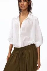 Pantalón globo verde militar de corte holgado en tejido con leve brillo, con elástico fruncido y cordón ajustable en la cintura, bolsillos laterales y puños abotonados en el bajo.