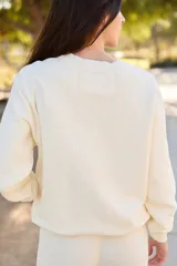 Sweater de tejido de punto color crema, con cuello redondo y manga larga. Estampado frontal con botas de cowboy amarillas y texto que dice "Boots Class and Little Sass".