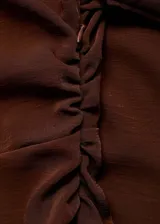 Vestido midi de color marrón chocolate, con diseño asimétrico de un solo hombro, manga larga con puños elásticos y fruncidos, y silueta ajustada.