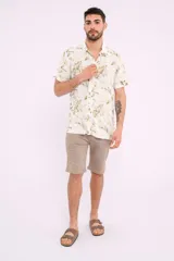 Camisa blanca con estampado de hojas verdes y marrones, de manga corta y cuello clásico.