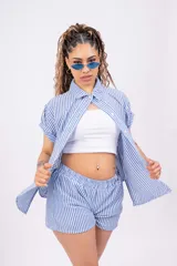 Conjunto de camisa y shorts a rayas verticales celestes y blancas. La camisa es de manga corta y se usa abierta sobre un top blanco.