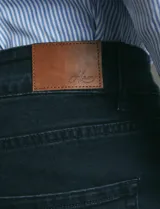 Pantalon denim de cinco bolsillos, corte recto y color negro, con botones y remaches metálicos en tono plata viejo.