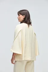 Capa de lana fina sin teñir, con diseño de corte amplio y mangas tipo kimono. Presenta cierre frontal mediante tres alamares de cuero en tono marrón.