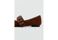 Zapatos planos de gamuza marrón, con punta fina, cierre de dos tiras con hebillas metálicas en el empeine y detalle de lazo pequeño en la puntera.