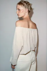 Blusa de punto color beige con cuello barco, manga larga abullonada con puños ajustados y detalles fruncidos en la parte delantera.