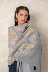 Pashmina de tela densa y suave, con caída pesada y diseño bordado con motivos florales en tonos dorados y beige. Presenta terminaciones con flecos en los extremos.