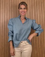 Blusa rosada de algodón con delicados bordados florales blancos, escote en V con cuello elevado y volados, y mangas largas con puños acampanados.
