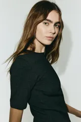 Vestido corto de punto con escote redondo y mangas cortas. Presenta un diseño entallado en el cuerpo y una falda con volado inferior confeccionado en tela satinada con brillo.