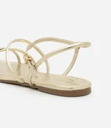 Sandalia plana dorada con tiras finas y cierre con hebilla en el tobillo.